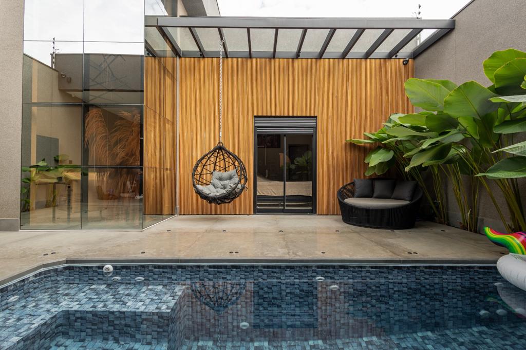 Área de piscina com fechamento de vidro e painel ripado